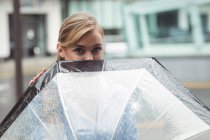 Bella donna guardando fuori da ombrello durante la stagione delle piogge — Foto stock