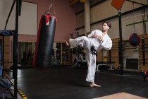 Vista lateral del hombre practicando karate con saco de boxeo en gimnasio - foto de stock