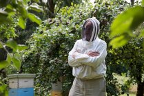 Beekeeper standing with arms crossed in apiary garden — Stock Photo