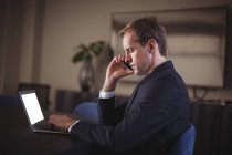 Empresário falando ao telefone enquanto usa laptop no escritório — Fotografia de Stock