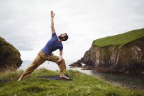 Человек, выполняющий упражнения на растяжку на скале — стоковое фото