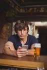 Человек, использующий мобильный телефон со стаканом пива на столе в баре — стоковое фото