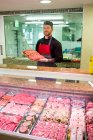 Macellaio in piedi al banco della carne in macelleria — Foto stock