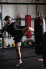 Vista lateral do Boxer praticando boxe com saco de perfuração no estúdio de fitness — Fotografia de Stock