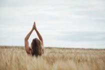Visão traseira da mulher de pé com as mãos levantadas sobre a cabeça em posição de oração no campo no dia ensolarado — Fotografia de Stock