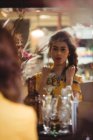 Donna che indossa una collana vintage e si guarda allo specchio nel negozio di antiquariato — Foto stock