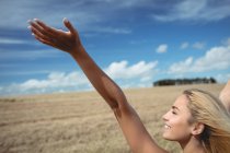 Rear view of happy blonde woman standing in field with open arms — Stock Photo