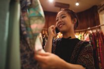 Жінка розмовляє на мобільному телефоні під час вибору одягу на вішалках в магазині одягу — стокове фото