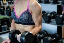 Mi-section de femme soulevant haltères à la salle de gym — Photo de stock