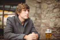Thoughtful man sitting in bar with glass of beer on table — Stock Photo
