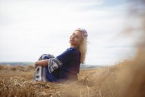 Sorrindo mulher loira sentada em campo e olhando para a câmera — Fotografia de Stock