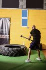 Rückansicht eines thailändischen Boxers, der im Fitnessstudio mit dem Vorschlaghammer auf Reifen einschlägt — Stockfoto