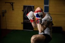 Tattooed Thai boxer practicing boxing in gym — Stock Photo