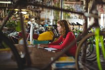 Woman sitting at table and using computer in bicycle shop — Stock Photo