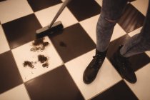Sezione bassa di parrucchiere femminile che pulisce i rifiuti dei capelli sul pavimento con scopa nel salone — Foto stock