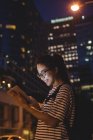 Mujer joven usando tableta digital en la calle por la noche - foto de stock