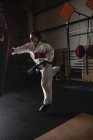 Женщина практикует карате с боксерской грушей в темной студии фитнеса — стоковое фото