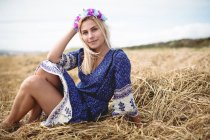 Безтурботна блондинка в блакитній сукні сидить у полі і дивиться на камеру — стокове фото