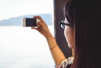 Primer plano de la mujer tomando fotos en el teléfono móvil desde el barco - foto de stock