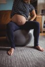 Geschnittenes Bild einer schwangeren Frau, die im Wohnzimmer Dehnübungen auf einem Fitnessball durchführt — Stockfoto