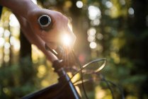 Manos de atleta masculino de pie con bicicleta de montaña en el parque a la luz del sol - foto de stock