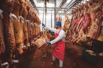 Macellaio che appende carcasse di carne rossa nel magazzino della macelleria — Foto stock