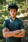 Портрет велосипедиста мужского пола, стоящего со скрещенными в лесу руками — стоковое фото