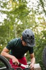Мужчина-велосипедист чинит свой велосипед в лесу в солнечный день — стоковое фото