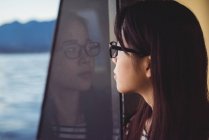 Nachdenkliche junge Frau schaut während Schiffsreise durch Fenster — Stockfoto
