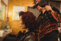 Peluquero secador de pelo pelo del cliente en un salón profesional - foto de stock