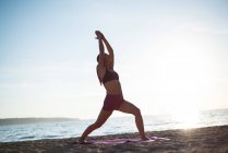 Baixo ângulo de visão da mulher realizando ioga na praia no dia ensolarado — Fotografia de Stock