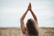 Woman with hands raised over head in prayer position in field on a sunny day — Stock Photo