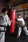 Sportiva e sportiva che pratica karate con sacco da boxe in studio — Foto stock