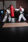 Uomo e donna che praticano karate con sacco da boxe in studio — Foto stock