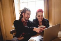 Smiling couple using laptop while sitting at table — Stock Photo