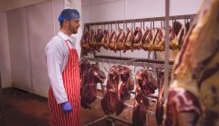 Carniceiro olhando para o coração de carne pendurado na sala de armazenamento no açougue — Fotografia de Stock