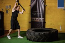 Thai boxer hitting tire with sledge hammer in fitness studio — Stock Photo