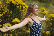Woman standing with arms outstretched in meadow on sunny day — Stock Photo