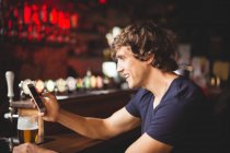 Man with glass of beer using mobile phone in counter at bar — Stock Photo