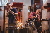 Glassblowers shaping a glass on the blowpipes at glassblowing factory — Stock Photo