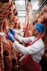 Metzger klebt ein Etikett auf das rote Fleisch, das in einem Abstellraum der Metzgerei hängt — Stockfoto