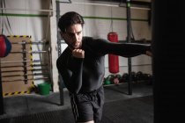 Retrato de Boxer masculino praticando boxe com saco de perfuração em estúdio de fitness — Fotografia de Stock