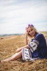 Беззаботная блондинка сидит в поле и смотрит в камеру — стоковое фото