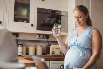 Mulher grávida bebendo água na cozinha em casa — Fotografia de Stock