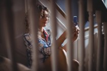 Beautiful woman sitting on staircase using mobile phone at home — Stock Photo