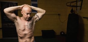 Vue panoramique du boxeur thaï tatoué et torse nu posant dans la salle de gym — Photo de stock