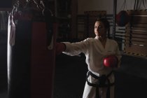 Femme pratiquant le karaté avec sac de boxe dans un studio de fitness — Photo de stock
