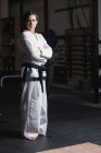 Portrait of woman in karate kimono standing with crossed arms in fitness studio — Stock Photo