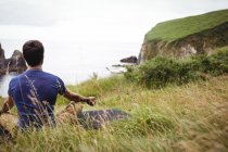 Vue arrière de l'homme effectuant le yoga sur la falaise — Photo de stock