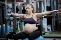 Mujer embarazada que preforma el ejercicio de estiramiento en la pelota de fitness en el gimnasio - foto de stock